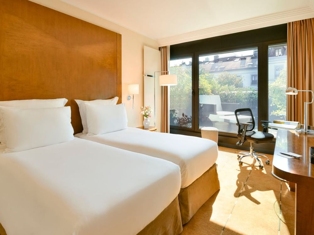 Twin beds by a wooden desk and a rolling chair in Deluxe Terrace Room at Warwick Geneva