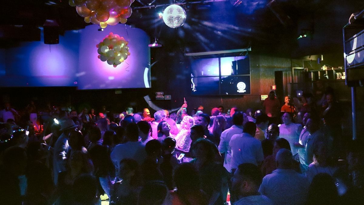 Invitados bailando en una fiesta llena de gente bajo luces de discoteca y globos en El Rollo de Araiza Palmira