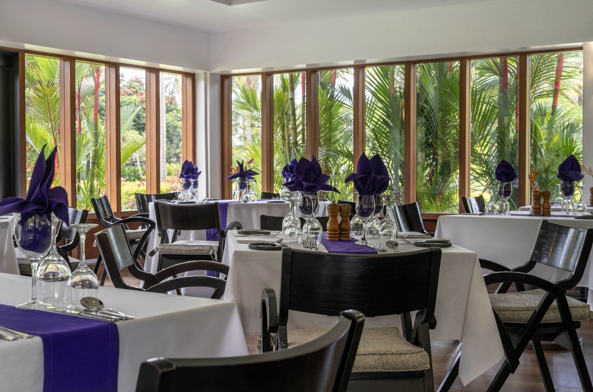 Dining tables with purple napkins by large windows under a white ceiling in Talei Restaurant at The Naviti Resort - Fiji