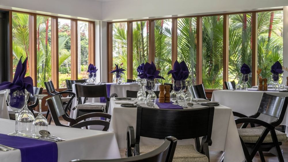 Dining tables with purple napkins by large windows under a white ceiling in Talei Restaurant at The Naviti Resort - Fiji