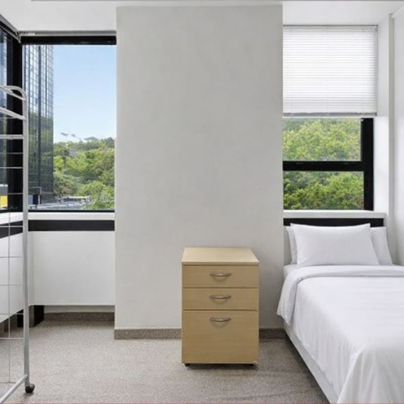 A clean room with a bed, drawers, and two windows at UniLodge Stafford House.