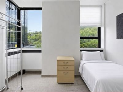 A clean room with a bed, drawers, and two windows at UniLodge Stafford House.