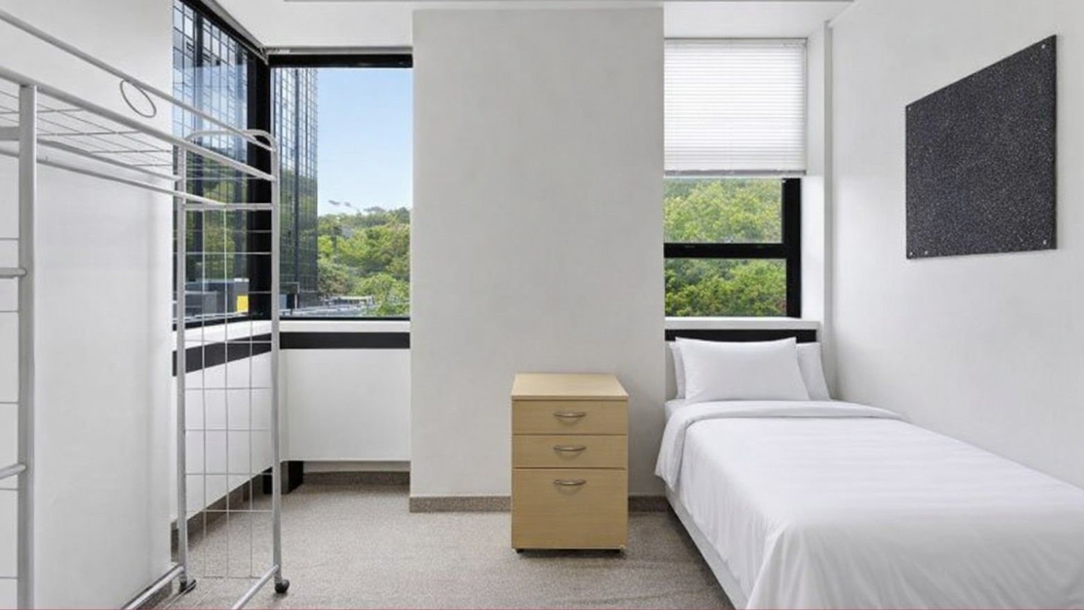 Clean room with white bed, small drawers, and view of trees at UniLodge Stafford House.
