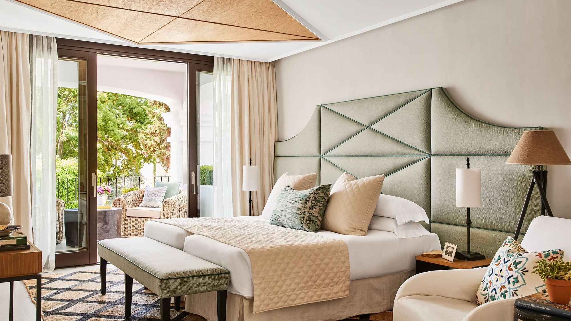 Santa Margarita Two-Bedroom Suite with a bed, woven rug, bench, & glass doors opening to patio at Marbella Club