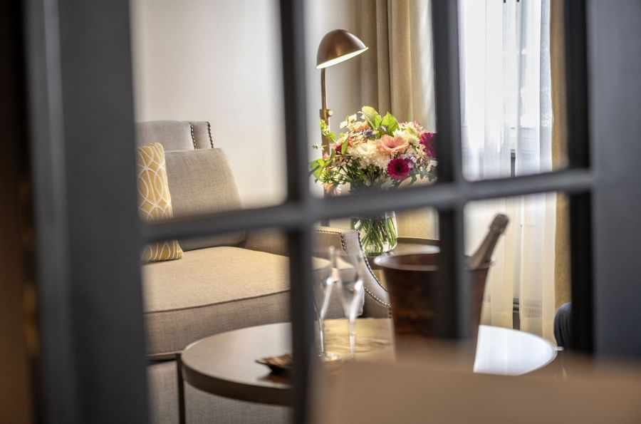 Lush floral vase by a grey armchair near a window under a warm brass lamp in Grand Suite at Warwick San Francisco