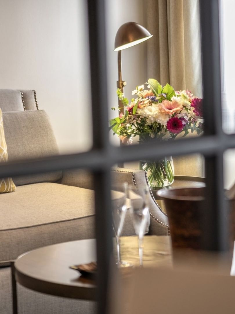 Lush floral vase by a grey armchair near a window under a warm brass lamp in Grand Suite at Warwick San Francisco