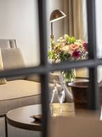 Lush floral vase by a grey armchair near a window under a warm brass lamp in Grand Suite at Warwick San Francisco