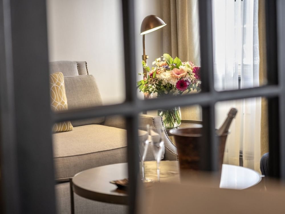Lush floral vase by a grey armchair near a window under a warm brass lamp in Grand Suite at Warwick San Francisco