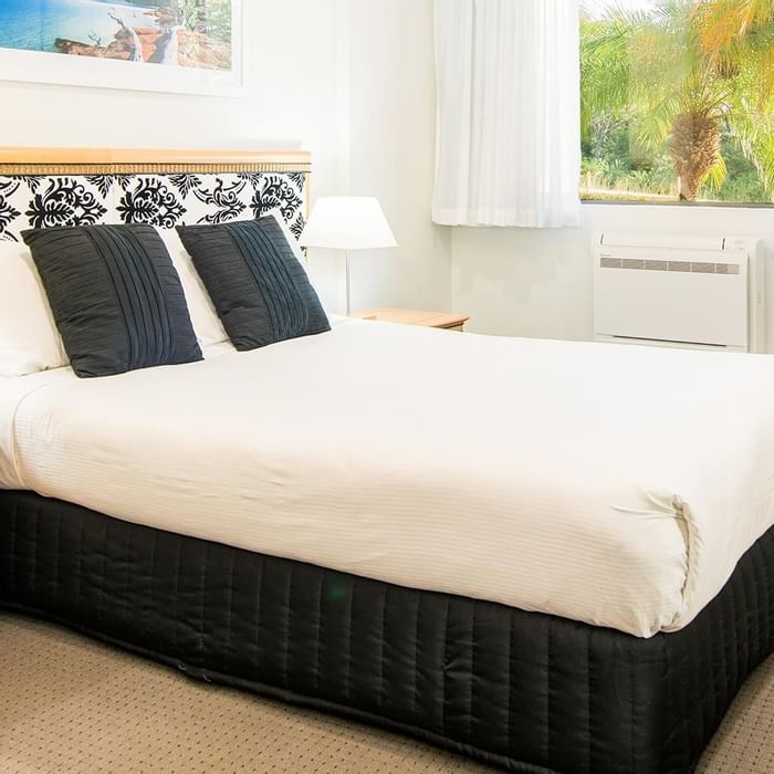Interior of a hotel room with a black and white patterned bed arrangement by a window at Mercure Charlestown