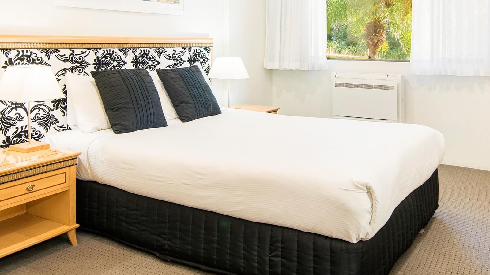 Interior of a hotel room with a black and white patterned bed arrangement by a window at Mercure Charlestown