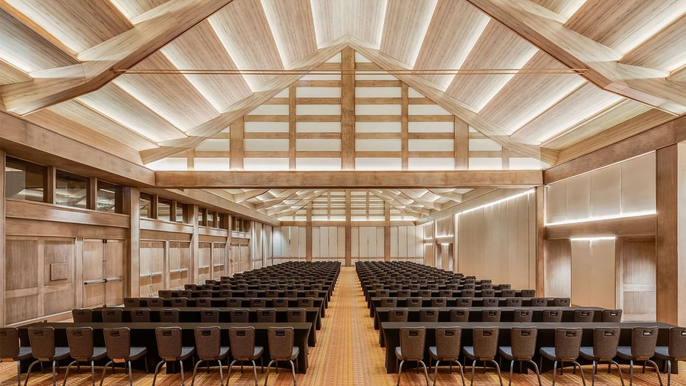 Spacious conference room with rows of tables and chairs under a wooden ceiling and warm lighting at Grand Fiesta Americana