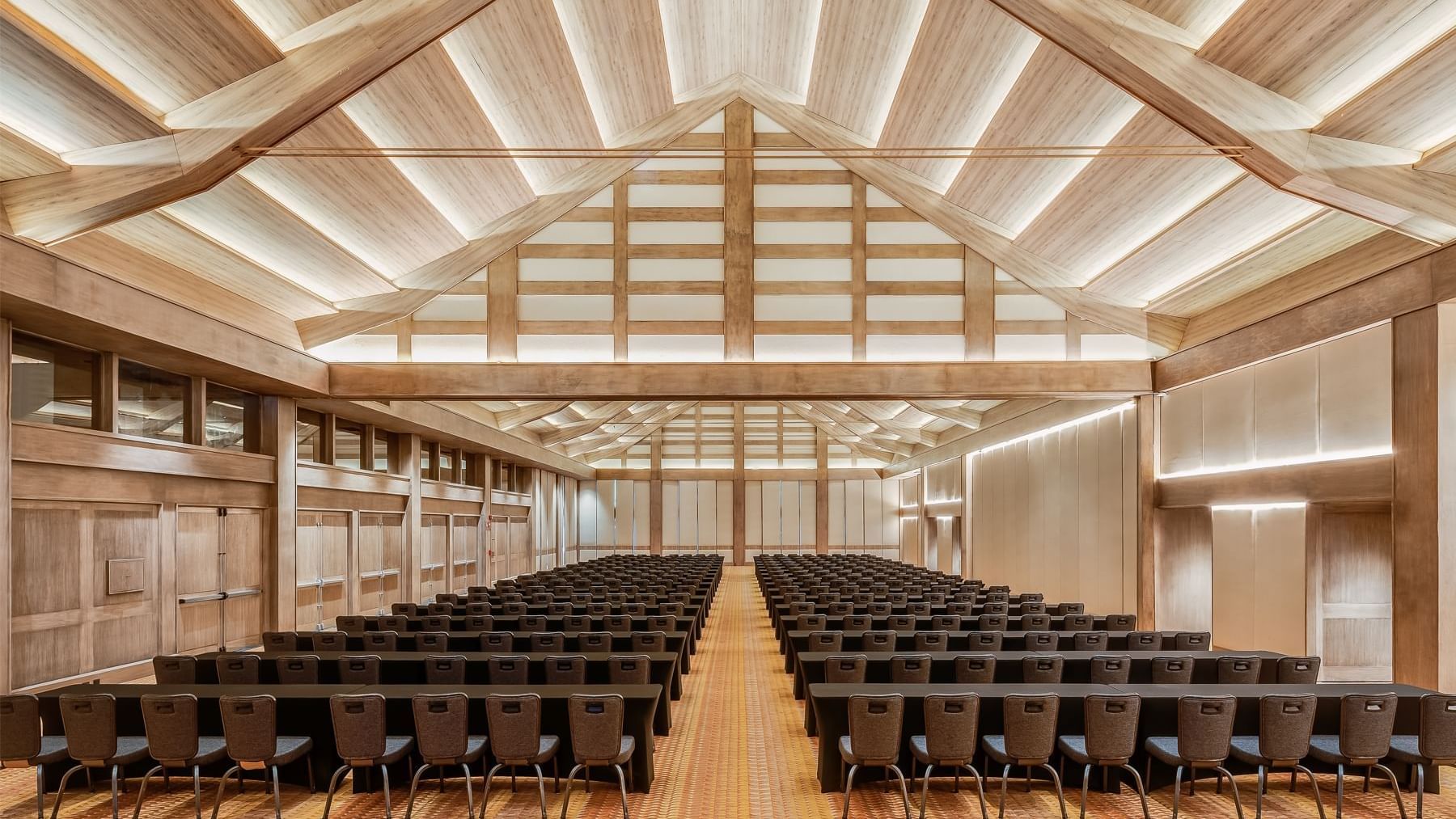 Spacious conference room with rows of tables and chairs under a wooden ceiling and warm lighting at Grand Fiesta Americana