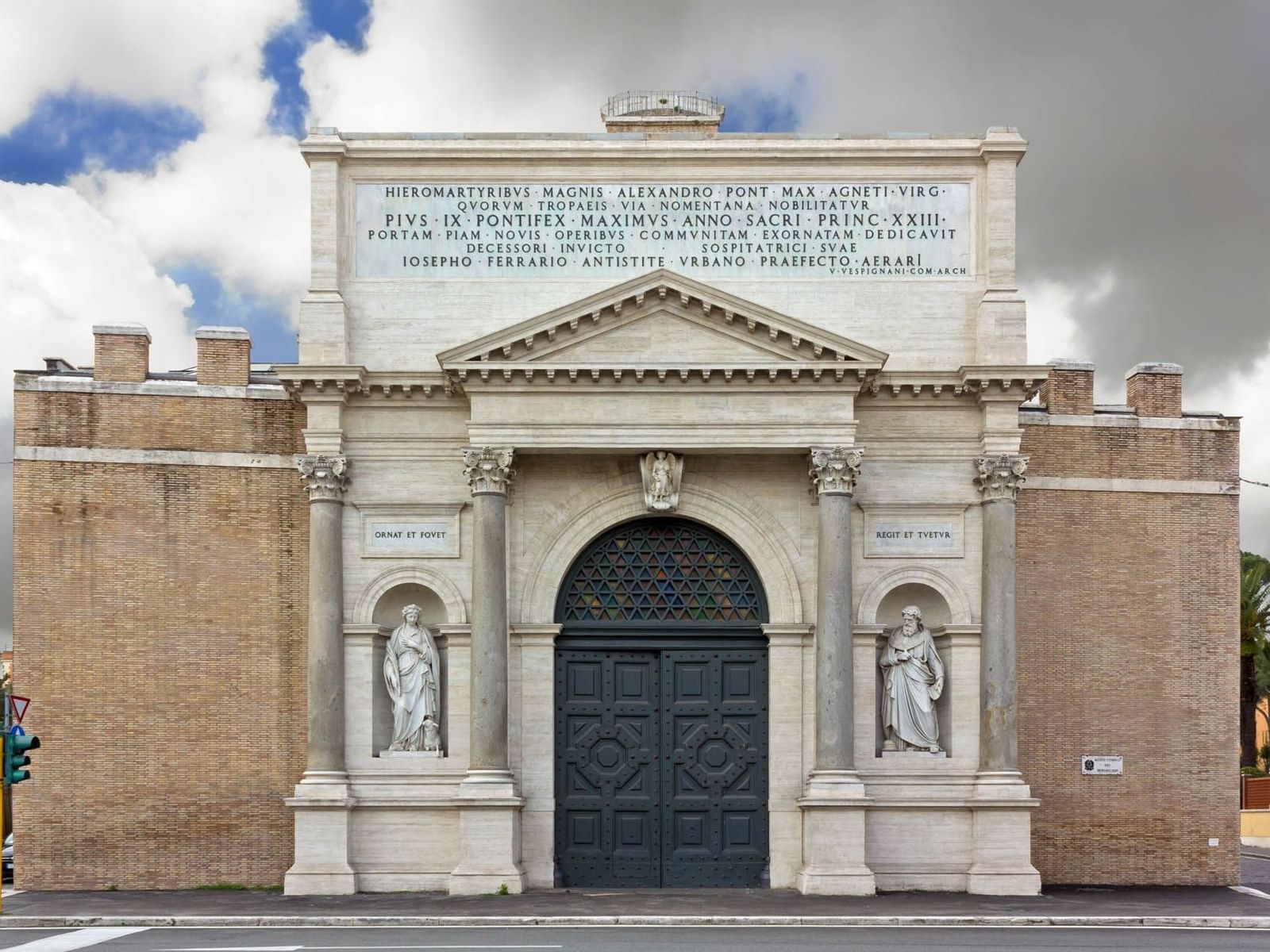 The grand facade of a Porta Pia featuring classical columns, intricate doors, and statues near The Glam Hotel