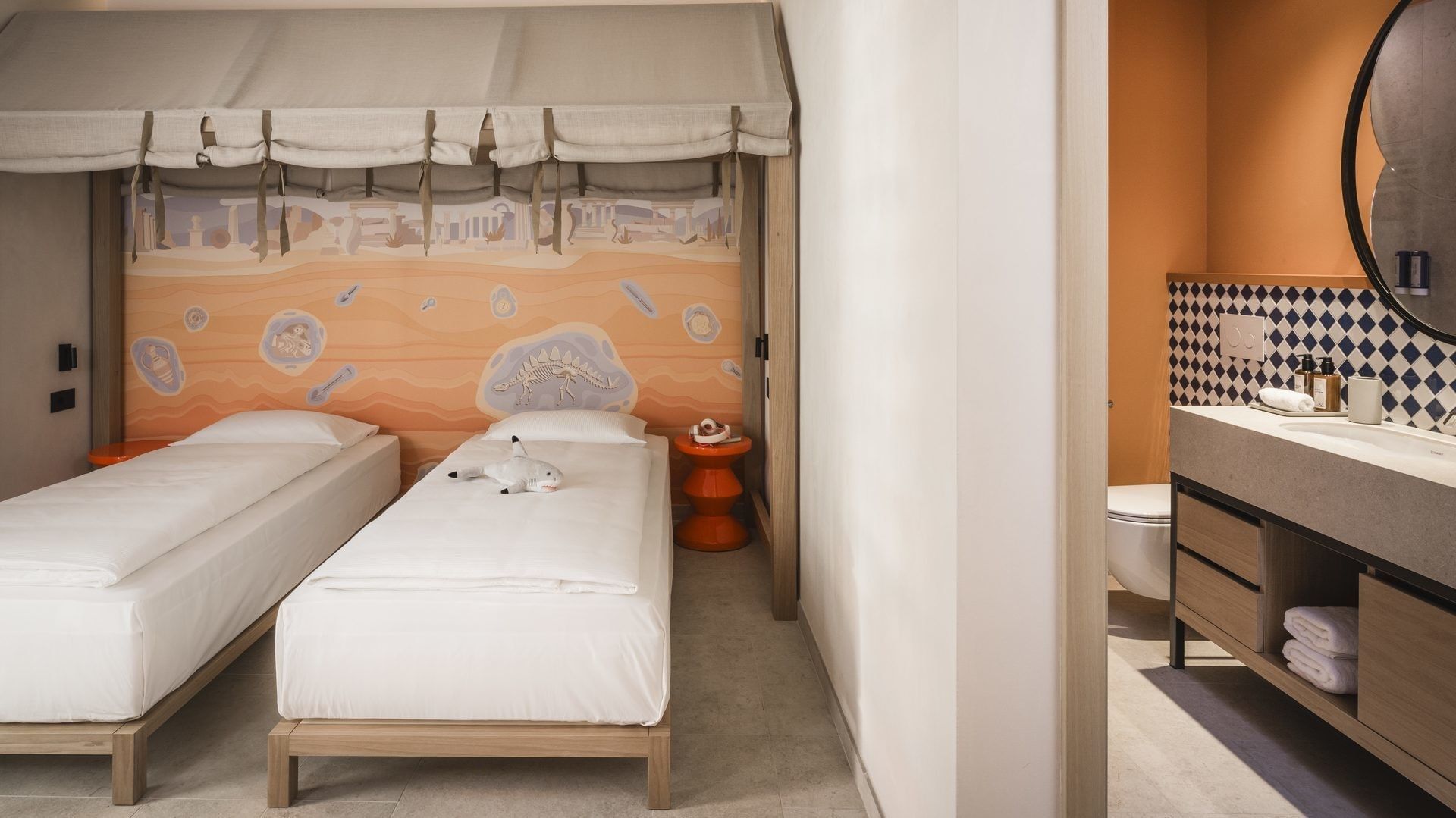 Due letti sotto una tenda, un bagno con un murale egiziano, e un bagno con un lavabo e uno specchio.