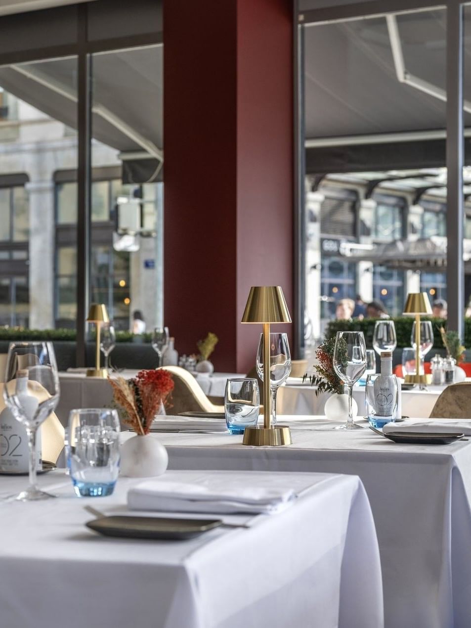 Elegant dining tables with gold lamps by large windows under a high ceiling in Téséo at Warwick Geneva