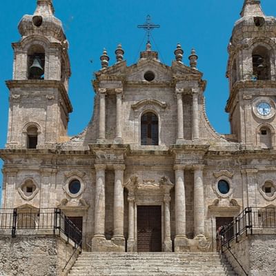 Antike Kirche mit zwei Glockentürmen, einer Uhr und einer Treppe vor einem blauen Himmel.