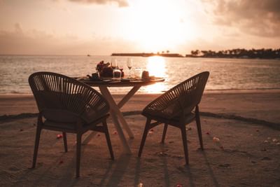 Private beach dining setup at sunset with two chairs, a flower-adorned table, and ocean views at Ananea Madivaru Maldives