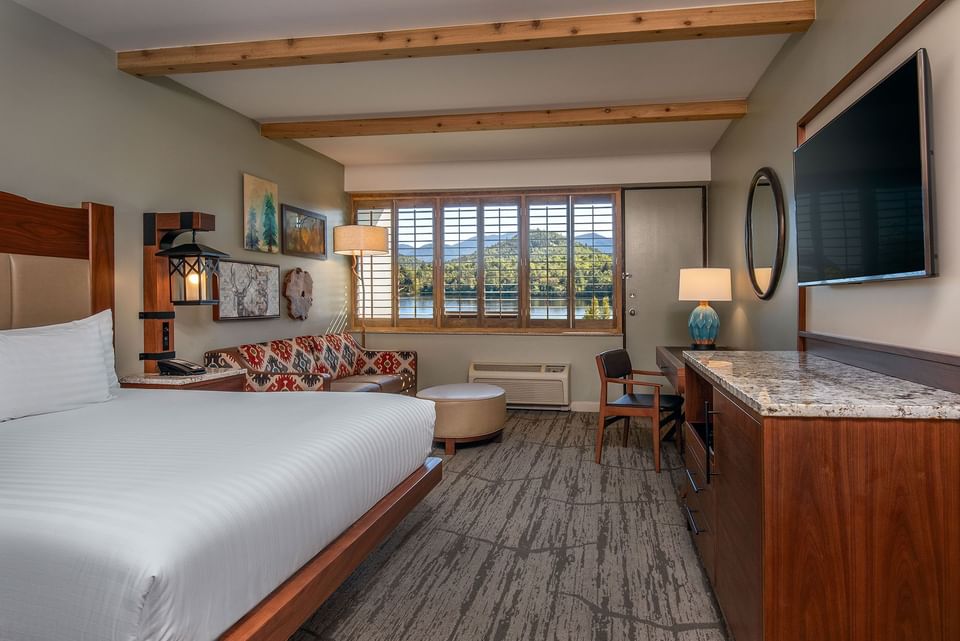 Bed by a patterned sofa under exposed wood beams, facing a lake window view in Premier View King at High Peaks Resort