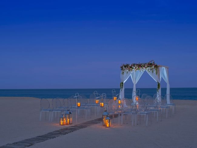 Wedding arrangements on the Beach with lanterns and an arch at dusk in Hacienda del Mar Los Cabos