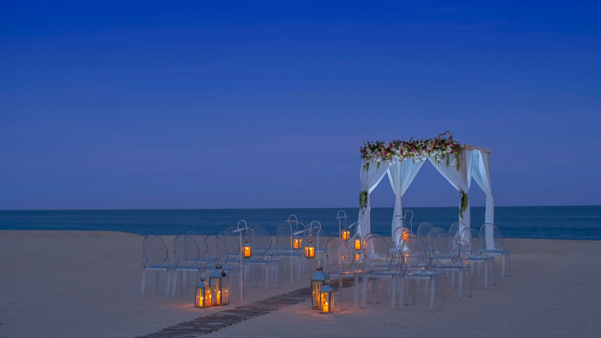Wedding arrangements on the Beach with lanterns and an arch at dusk in Hacienda del Mar Los Cabos
