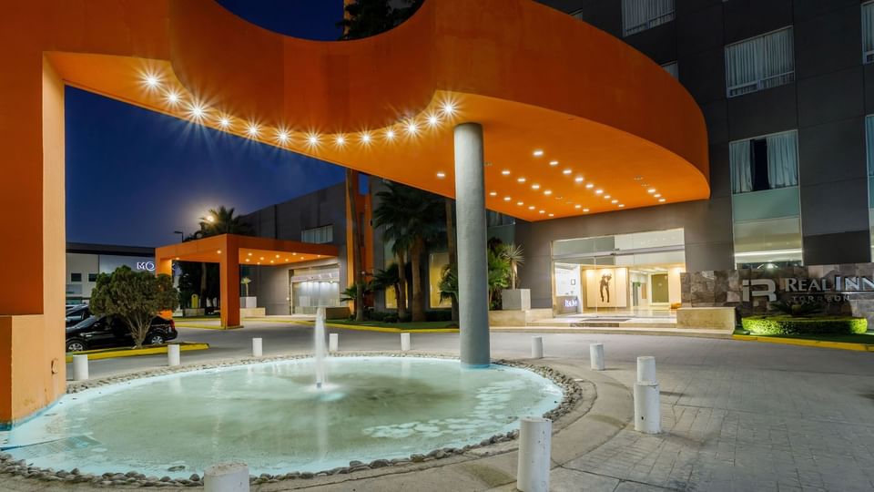 Vibrant orange architectural entrance with a circular fountain and bright night lighting at Real Inn Torreon