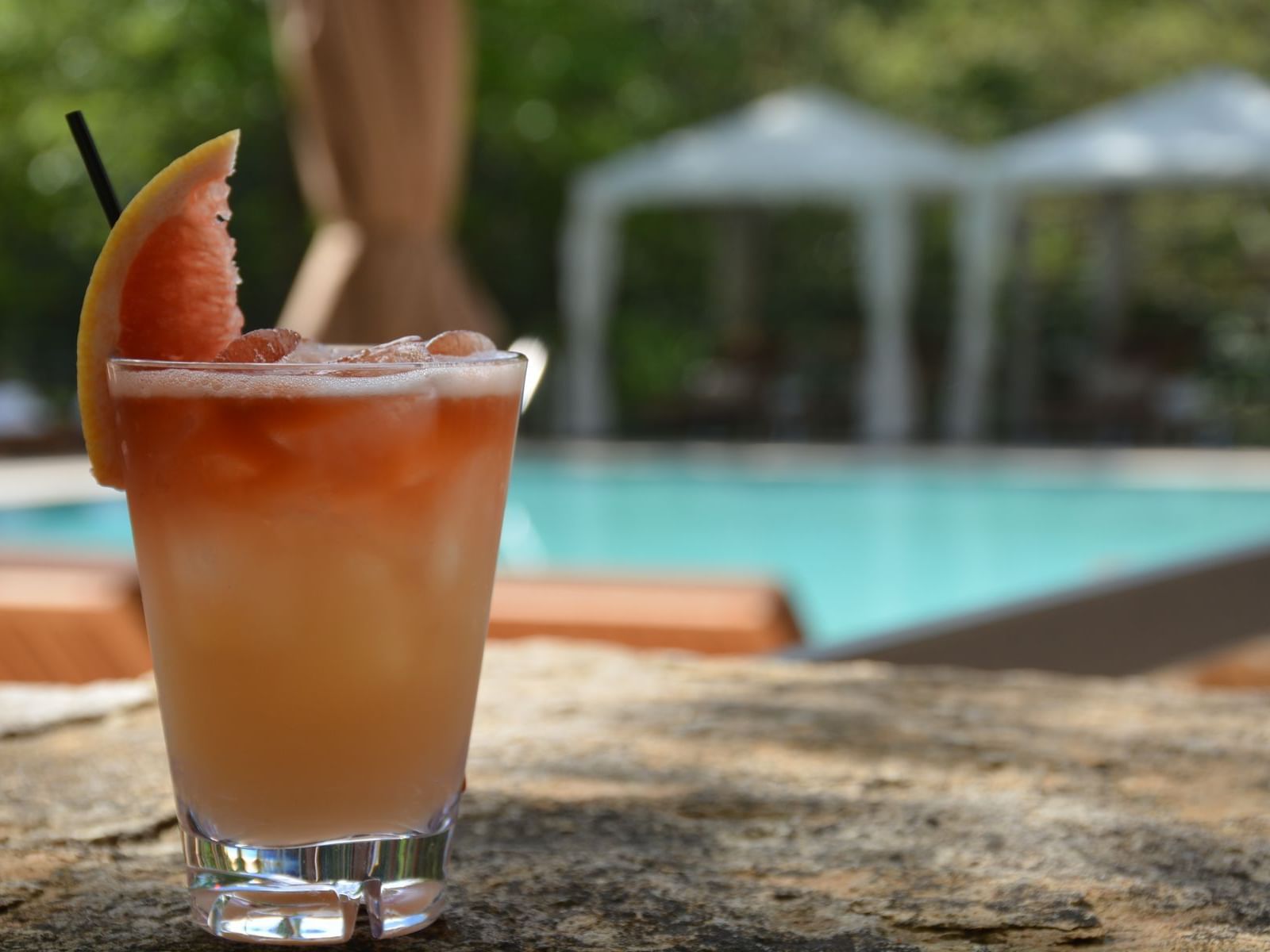 A refreshing drink with fruit & garnishes on a table by a pool at The Umstead Hotel and Spa