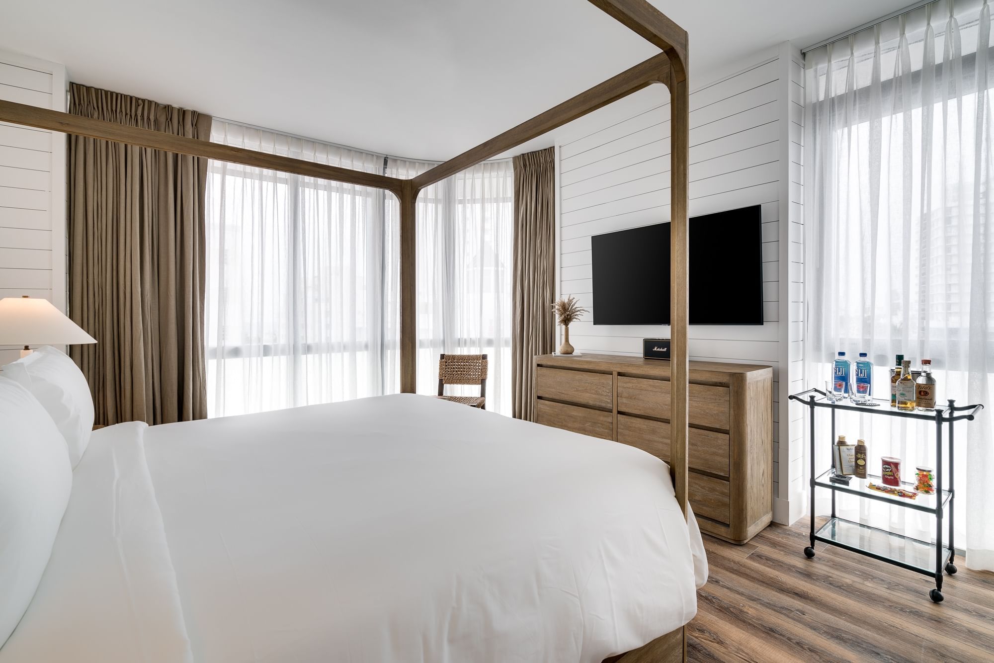 A wide view of a hotel room with a four-poster bed, dresser, TV, and minibar cart.