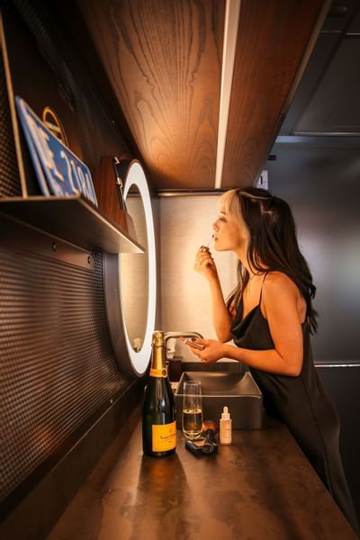 Woman applying lipstick while looking at mirror in Backstage at The Verb Hotel