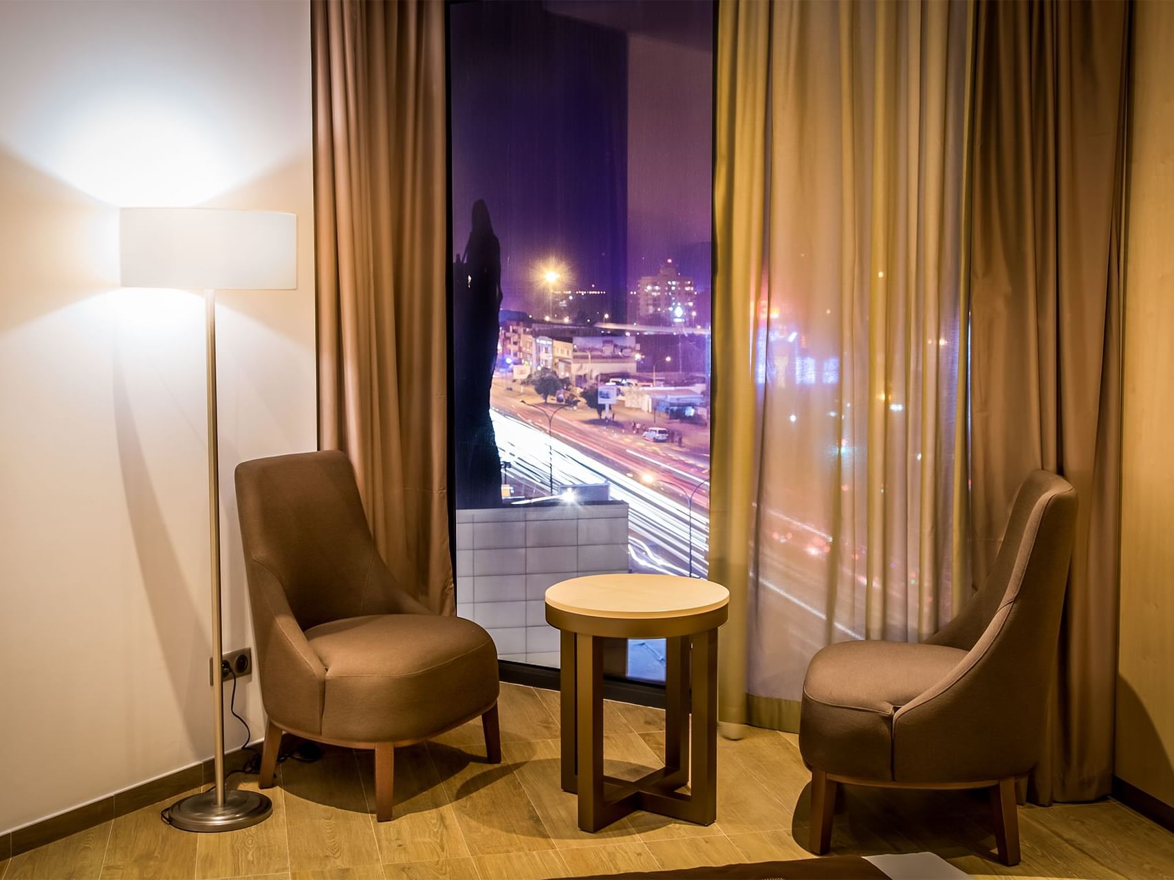 Two chairs and one coffee table with a window with the city view behind of Standard room in the Azalai Hotel Abidjan