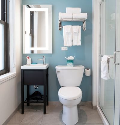 Modern bathroom with white vanity, toilet, glass shower, and neatly folded towels in the guest Room at Hotel Saint Clair