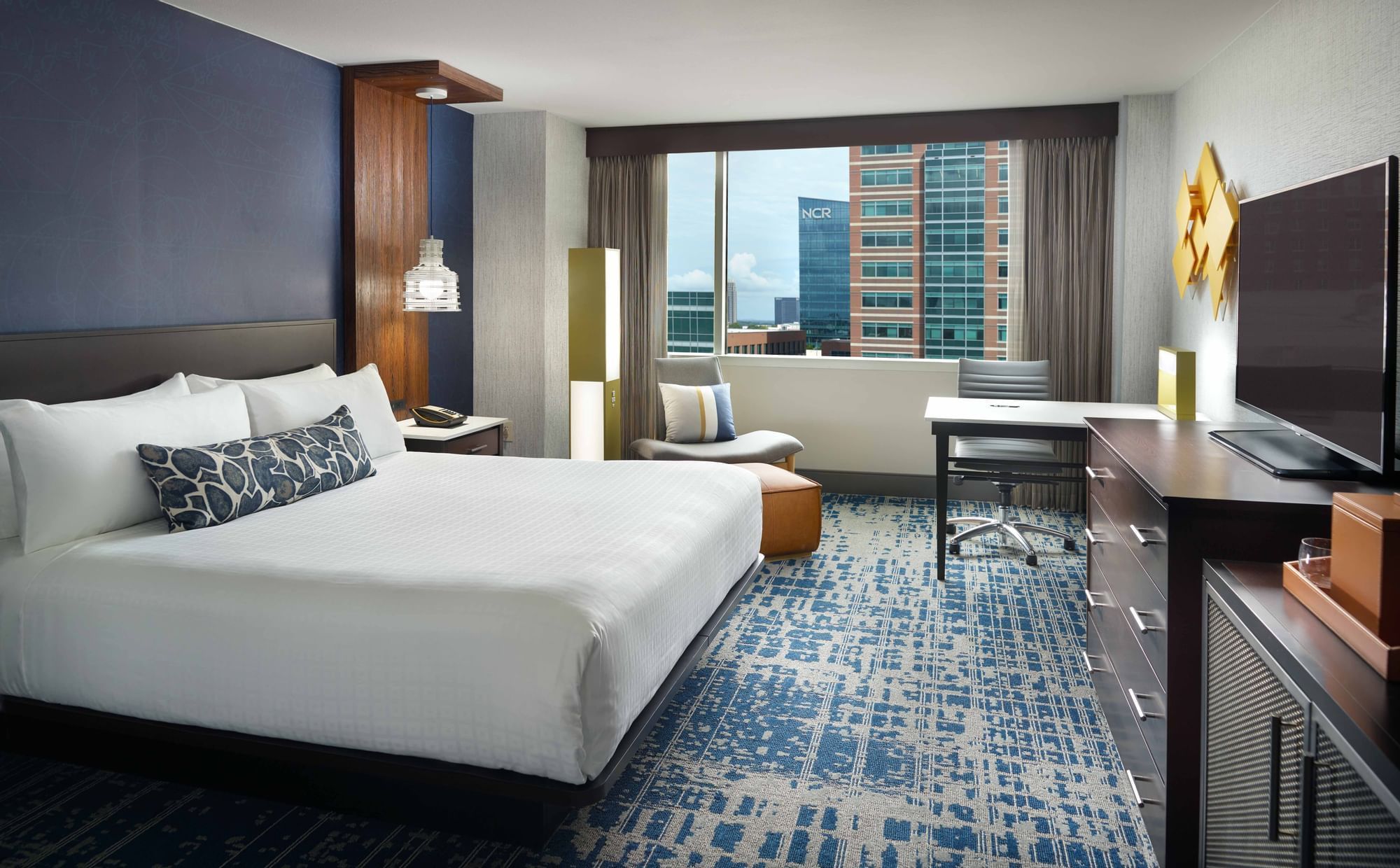 A hotel room with a large bed, desk, chair, and window.