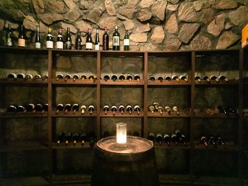 Cozy wine cellar with stone walls, a leather chair, and bottles of wine at La Cava de Santiago in Hacienda del Mar Los Cabos.