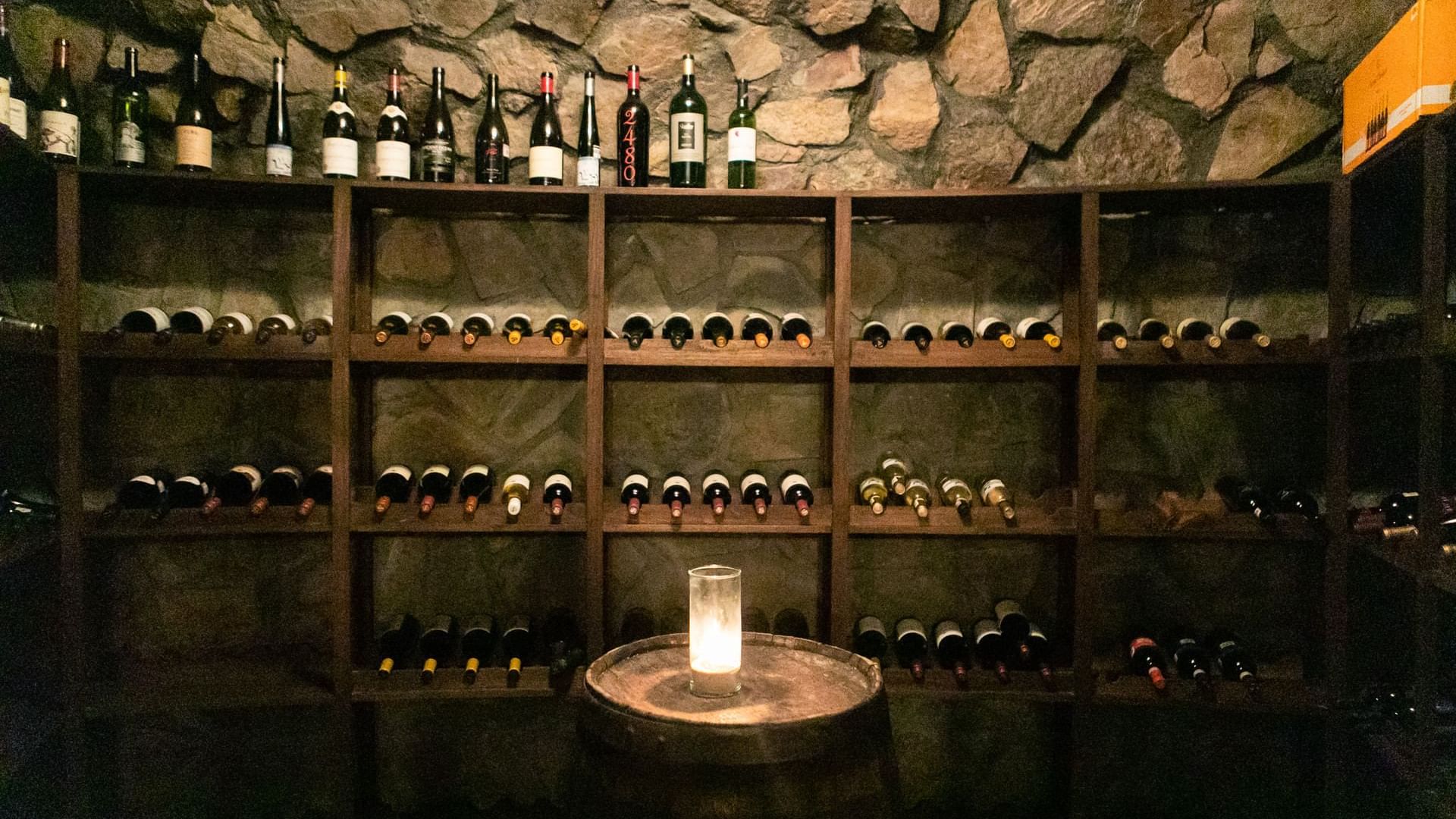 Cozy wine cellar with stone walls, a leather chair, and bottles of wine at La Cava de Santiago in Hacienda del Mar Los Cabos.
