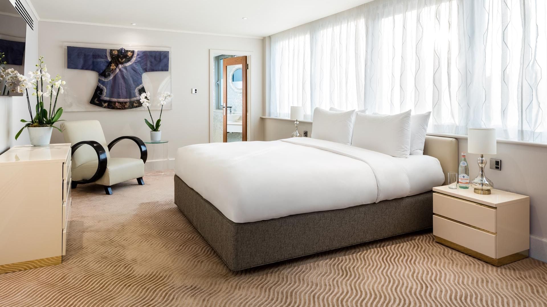 Bright Penthouse Suite at The May Fair Hotel with a large bed, patterned carpet, armchair, orchids, and modern décor