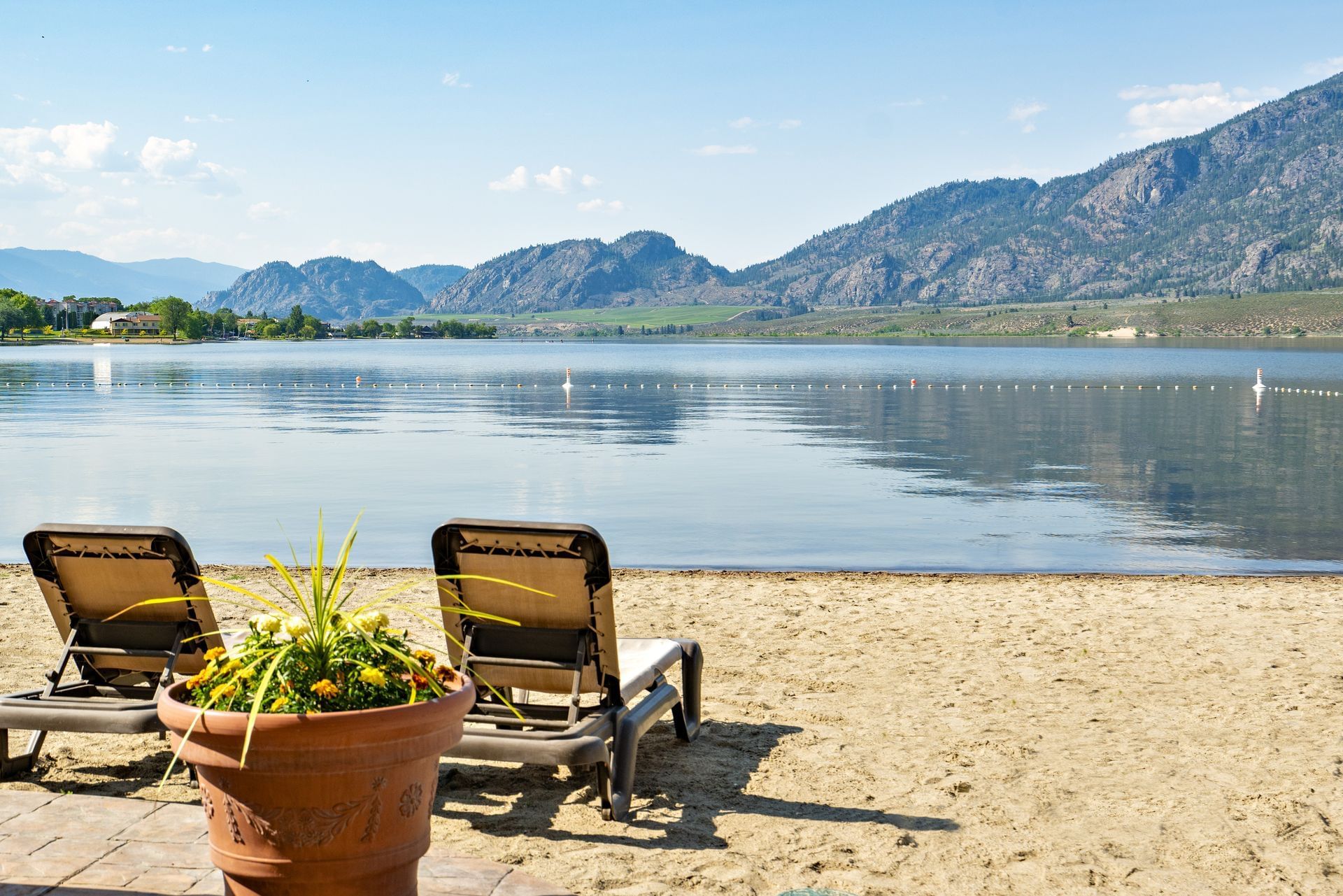 Two beach chairs on sand overlooking lake with mountains in back