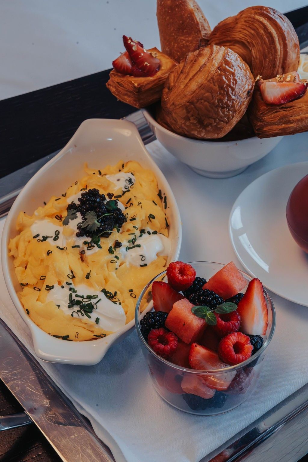 Scrambled eggs topped with caviar by a bowl of croissants and a cup of mixed berries at Hotel X Toronto