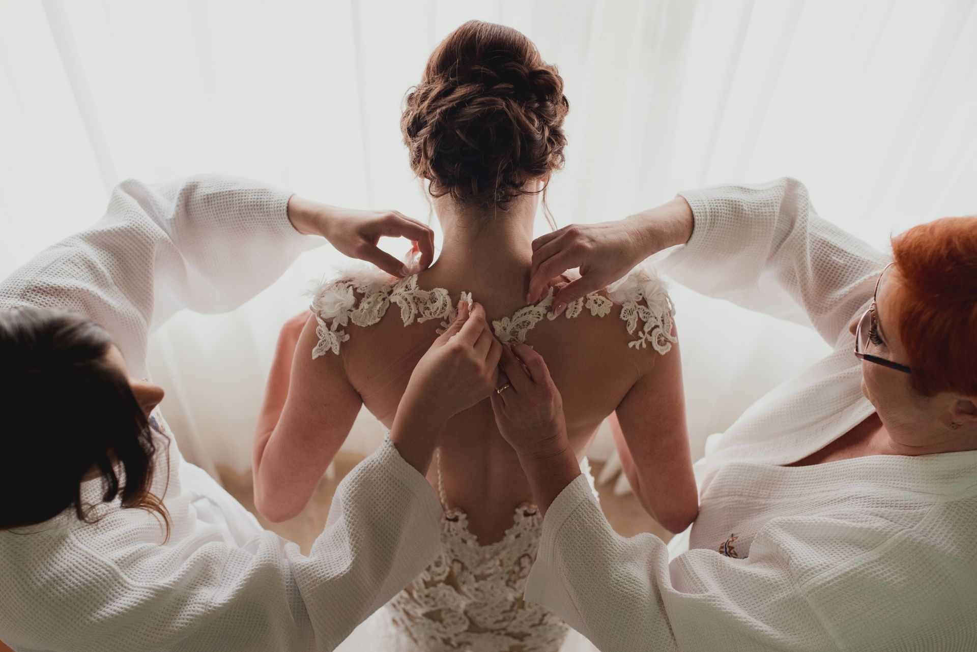 Bride is dressed in her gown and two assistants fasten the intricate lace detailing on her back at Sunset Plaza Beach Resort