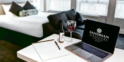 An image of a laptop with a pen and a notepad near wine bottle a