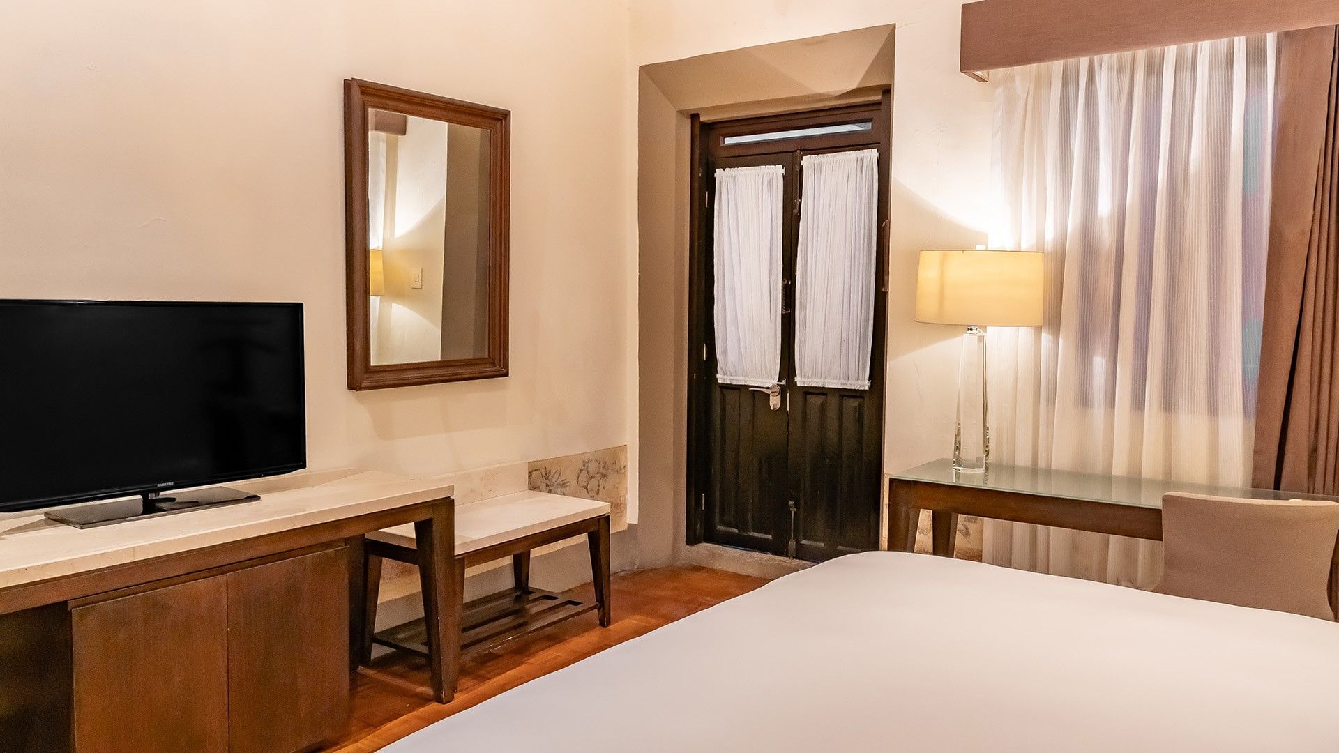 King New Class vanity area with a wooden mirror, glass-top desk, and a tall bedside lamp at Quinta Real Puebla