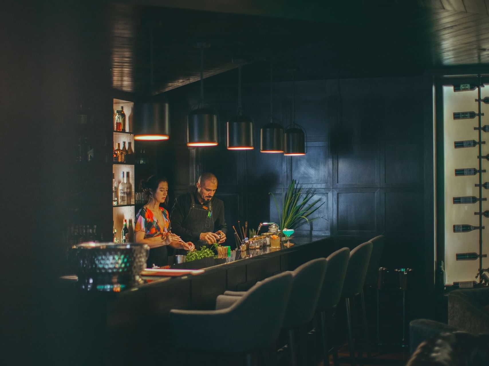 Bartender and a woman in Cocktail class with stools and shelves of bottles at El Silencio Lodge and Spa