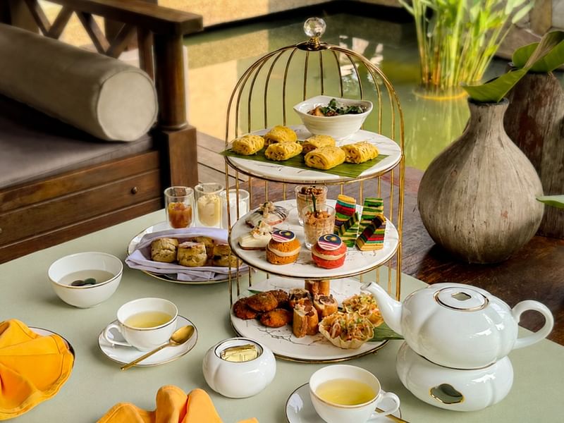 Three-tiered afternoon tea set with pastries, savory bites, and tea service arranged on a table at The Banjaran Hotsprings Retreat
