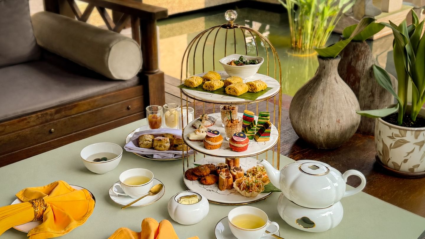 Three-tiered afternoon tea set with pastries, savory bites, and tea service arranged on a table at The Banjaran Hotsprings Retreat