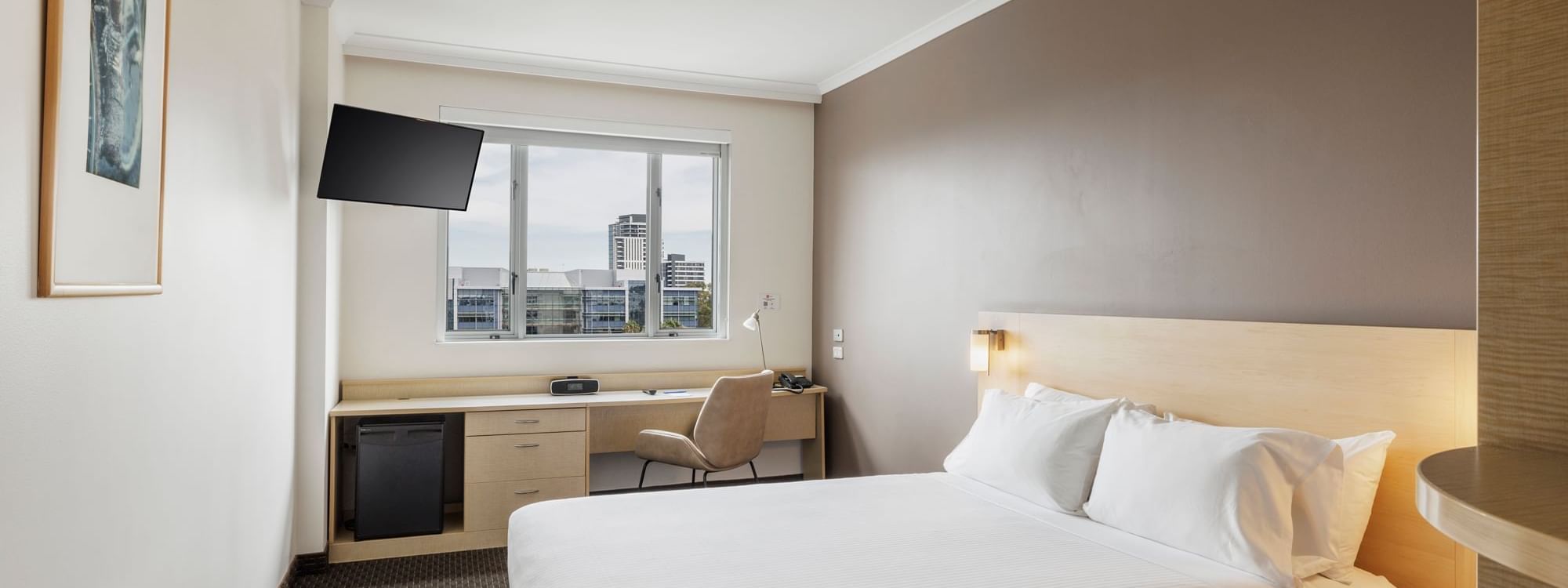 Work desk and TV by the bed in Standard King Room with a city view at Novotel Sydney Olympic Park