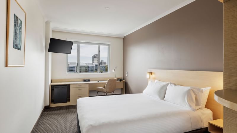 Work desk and TV by the comfy bed in Standard Queen Room with a city view at Novotel Sydney Olympic Park
