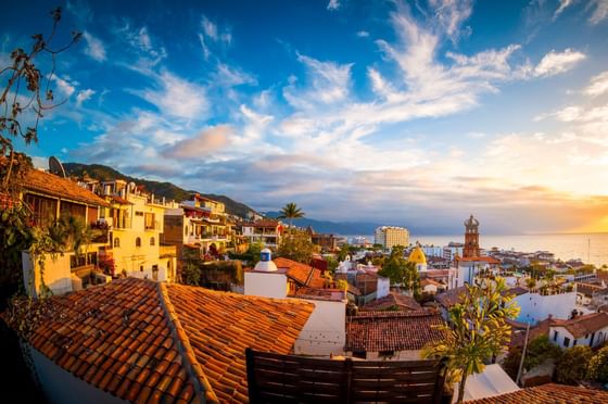 Tiled rooftops and hillside buildings facing the ocean under a bright blue sky with clouds at Los Arcos Suites