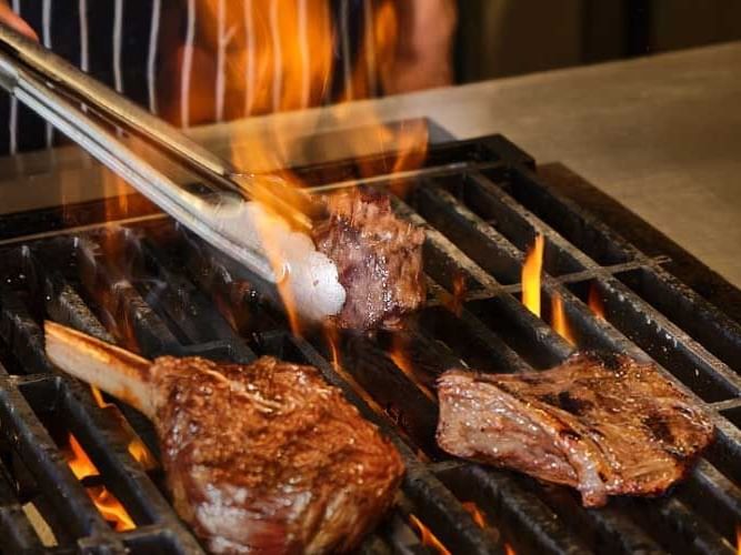 A chef skillfully grills steaks over an open flame, showcasing culinary expertise and vibrant cooking action.