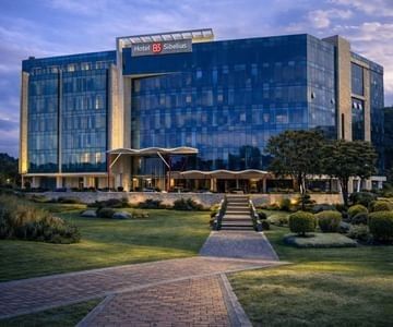 Modern glass building exterior with glowing lights under an evening twilight purple sky at Hotel B3 Sibelius