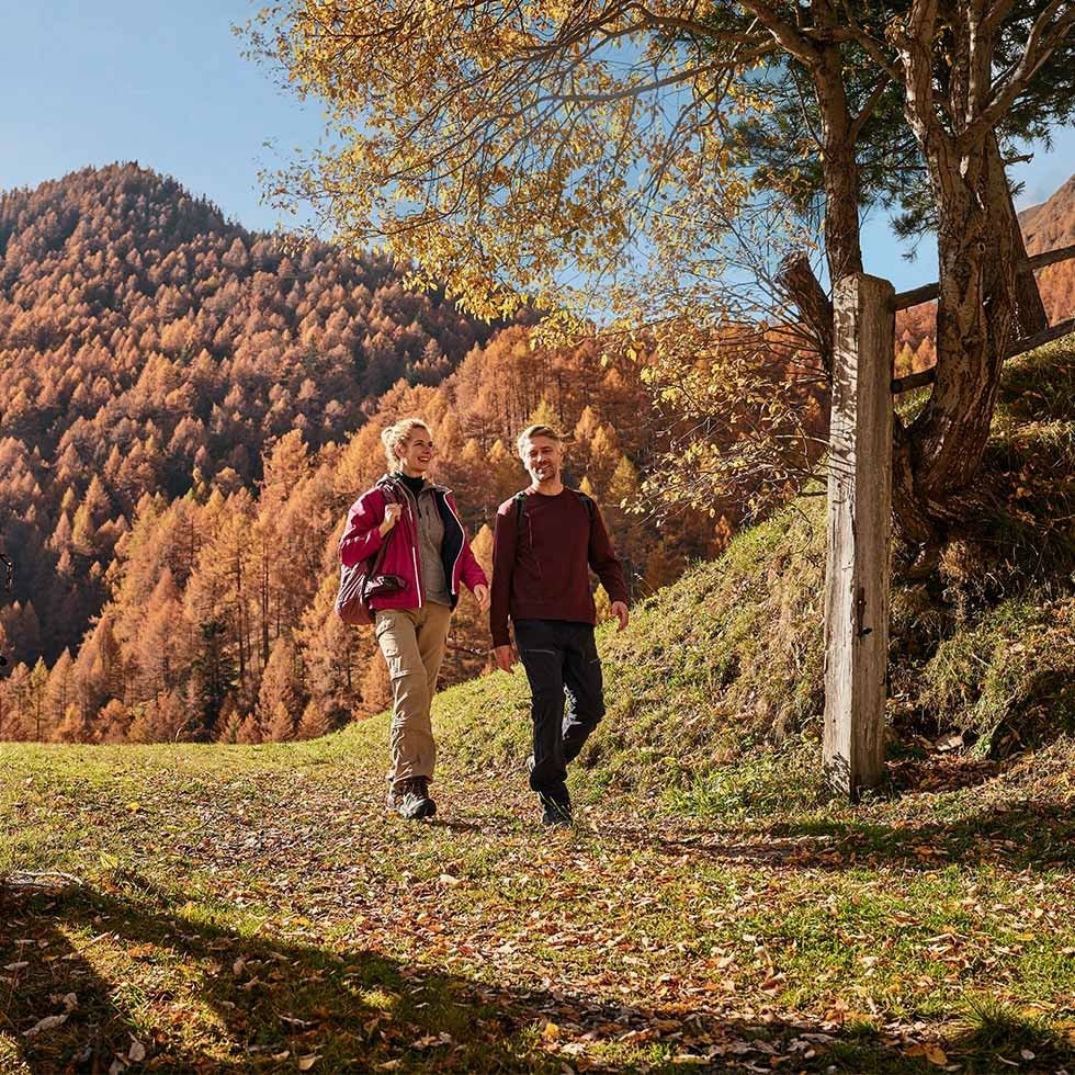 Couple walking on a trail in an autumn forest with colorful trees and mountains in the background.