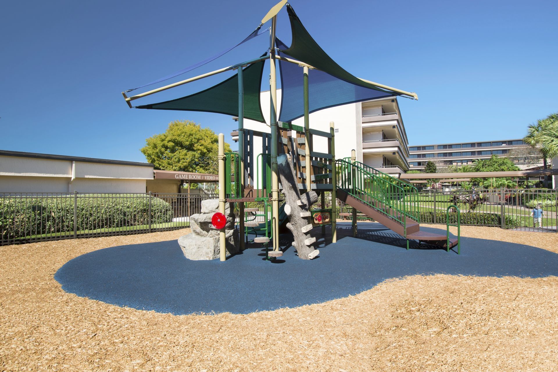 A playground with a green play structure and blue shade sail