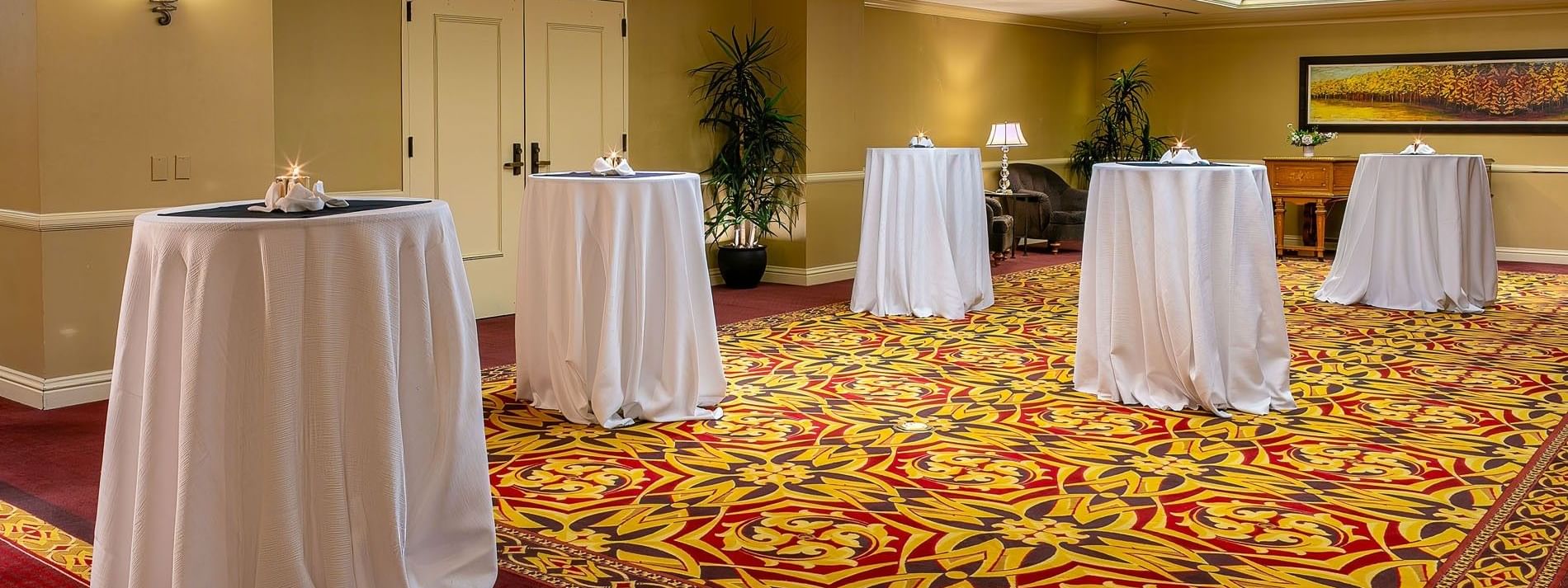 White cocktail tables by a wooden dresser on a patterned rug in Capitol Ballroom at Warwick Denver
